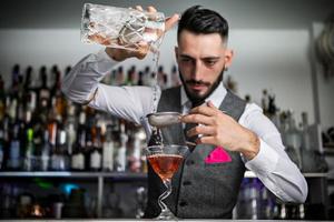 camarero con tamiz vertiendo bebida en vaso foto