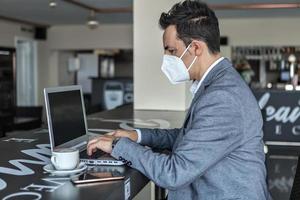 Businessman in protective mask using laptop in cafe photo