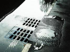 Water flowing into the sewer manhole. Wet road with sewer hatches. photo