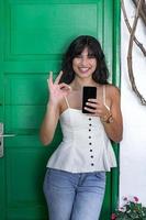 Optimistic Hispanic female with smartphone gesturing OK photo