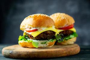Two fresh tasty homemade hamburgers with fresh vegetables, lettuce, tomato, cheese beside sliced tomatoes on a cutting board. Free space for text photo