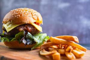 hamburguesa casera fresca y sabrosa con verduras frescas, lechuga, tomate, queso en una tabla para cortar con papas fritas. espacio libre para texto foto