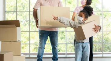 Mixed Race families are carrying cardboard boxes and walking from the front door into the house in a new house on moving day. Concept of relocation, rental, and homeowner moving at home. photo