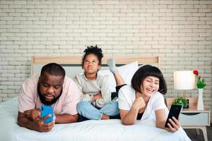 las niñas afroamericanas no están satisfechas y tristes, sentadas en medio entre padre y madre. los padres están usando el teléfono inteligente y los niños abandonados. los niños necesitan la atención de sus padres.