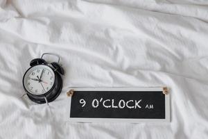 Alarm clock on the bed with sign board saying 9 oclock AM photo