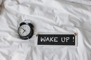 Alarm clock with wake up sign board on the bed photo