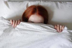 woman hiding face from sunlight under bed cover photo