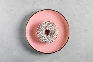 donut con cobertura de coco se encuentra en un plato de cerámica rosa