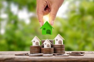 mano que sostiene el modelo de casa pequeña verde colocado en la pila de monedas de concepto de bienes raíces de inversión foto