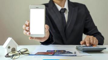 empresario sosteniendo un teléfono celular con una pantalla blanca e informes financieros en su escritorio foto