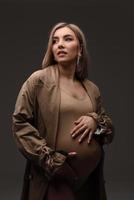 Stylish beautiful pregnant woman in a raincoat holds her hands on her stomach. photo