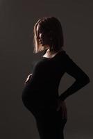 elegante hermosa mujer embarazada con un vestido negro sostiene sus manos sobre su estómago. foto