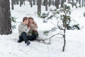 Bride and groom in beige knitted pullovers in snowy forest. Newlyweds is touching foreheads. Winter wedding. Copy space photo
