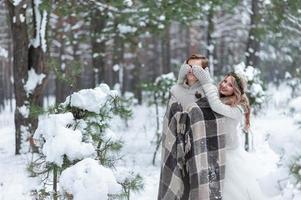 linda chica cubriendo los ojos de su novio con sus guantes de punto. boda de invierno.