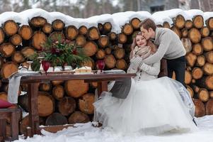 Groom is tenderly hugs his bride from the back on background of winter wedding decoration photo