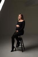 Stylish beautiful pregnant woman in a black dress holds her hands on her stomach. photo