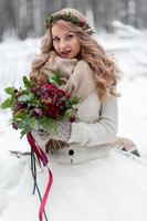 A young girl of Slavic appearance with a wreath of wildflowers. Beautiful blonde bride holds a bouquet in winter background. photo