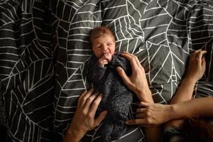 A little newborn boy is looking at the window in his crib. A boy born at 8 months of gestation. There is a knitted suit on the boy. photo