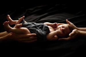 niño recién nacido sobre un fondo negro. la parte superior e inferior del niño sostienen las manos de los padres. foto