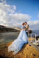 Wedding photo session of a couple on the seashore. Blue wedding dress on the bride.