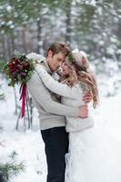 Bride and groom in beige knitted pullovers in snowy forest. Newlyweds is touching foreheads. Winter wedding. Copy space photo