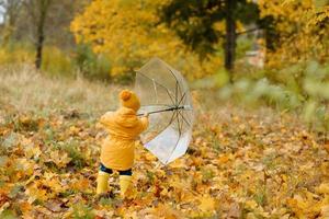 A little girl walks with an umbrella in yellow rubber boots and a waterproof raincoat. Autumn Walk. photo