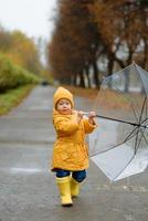 A little girl walks with an umbrella in yellow rubber boots and a waterproof raincoat. Autumn Walk.