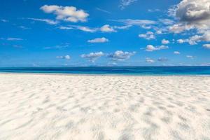 primer plano de la arena en la playa y el cielo azul de verano. paisaje panorámico de la playa. playa tropical vacía y paisaje marino. cielo azul, arena suave, calma, luz solar tranquila y relajante, estado de ánimo de verano. viaje de vacaciones foto