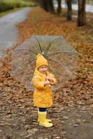 A little girl walks with an umbrella in yellow rubber boots and a waterproof raincoat. Autumn Walk. photo