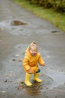 A little girl walks with an umbrella in yellow rubber boots and a waterproof raincoat. Autumn Walk. photo