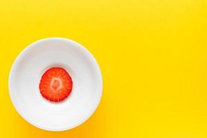 Slice of fresh strawberry on a round white plate on yellow background. Horizontal image seen from above. photo