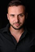 Studio portrait of a young caucasian man in a black blazer, looking at the camera, standing against plain studio background photo