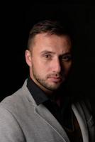 Studio portrait of a young caucasian man in a black blazer, looking at the camera, standing against plain studio background photo