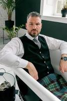 handsome mature courageous stylish man scotsman in kilt and suit laying in bathroom. Style, work from home, fashion, lifestyle, lockdown, culture, ethnic concept. photo