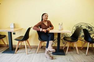 mujer afroamericana con camisa marrón y pantalón negro sentada en el café. foto