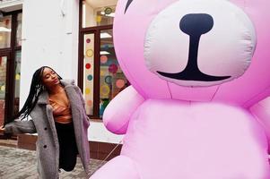 señora milenaria afroamericana cerca de oso de peluche rosa inflable. foto