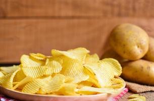 Potato chips snack on plate, Crispy potato chips on the kitchen table and fresh raw potatoes on wooden background