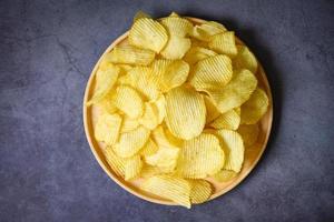 Potato chips snack on plate, Crispy potato chips on the kitchen table black background -  top view