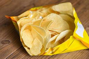 Potato chips on wooden background, Potato chips is snack in bag package wrapped in plastic ready to eat and fat food or junk food photo