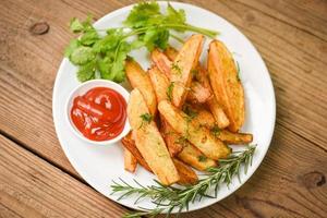 Potato wedges on white plate with rosemary herb coriander and tomato ketchup sauce, Cooking french fries or fry potatoes