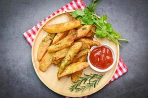 gajos de patata en un plato de madera con cilantro de hierbas de romero y salsa de ketchup de tomate, cocinando patatas fritas o patatas fritas foto