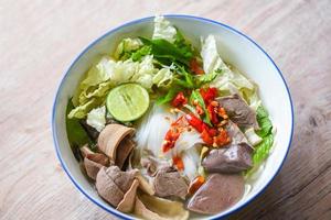 tazón de sopa de fideos pudín de sangre de cerdo y despojos de cerdo, fideos vermicelli de arroz tailandés con sopa clara y verduras frescas con brotes de limón salsa de chile de pimienta de frijol comida de menú tradicional tailandesa foto