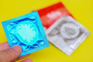 Condom in hand hold on yellow background - Colorful condom pack for birth control contraceptive means prevent pregnancy or sexually transmitted disease photo