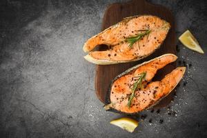 Grilled salmon steak with herbs and spices rosemary lemon on wooden cutting board background Cooked salmon fish fillet steak seafood photo
