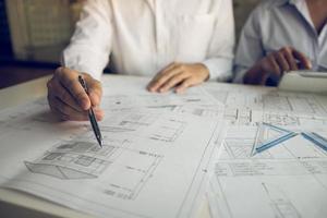 Architects engineer working with blueprints on table and discussing project together at the meeting in the office. photo