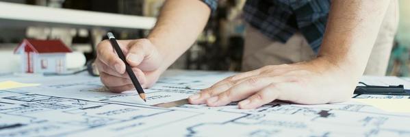 Interior designer or architect reviewing blueprints and holding pencil drawing on desk at home office. photo