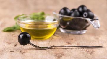 Olive oil with fresh herbs and olive on fork  on wooden background photo