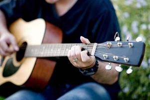 Picture of a guitarist, a young man playing a guitar while sitting in a natural garden,music concept photo