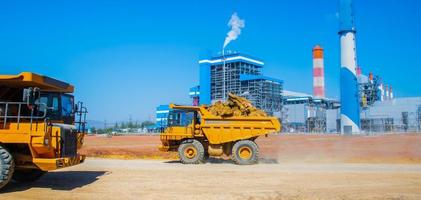 grandes camiones transportan mineral de las minas para alimentar las plantas industriales, detrás hay una planta de energía a carbón, los camiones están transportando. foto