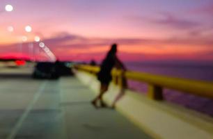 hermoso fondo de luces bokeh al atardecer, gente de pie en las barandillas del mar mirando al mar al atardecer. Cielo púrpura foto